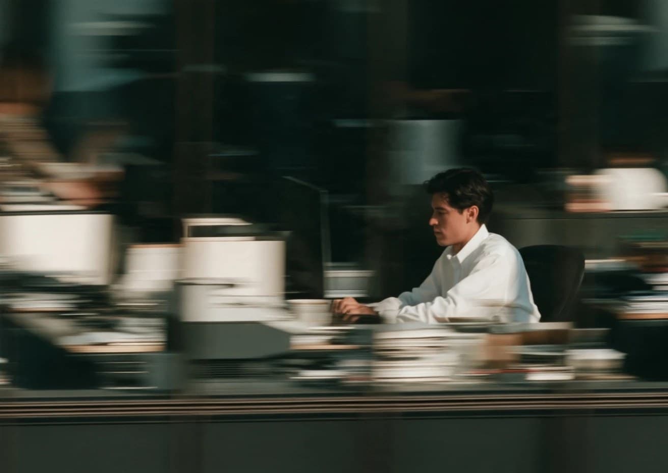 A man works at his desk while the office rushes past